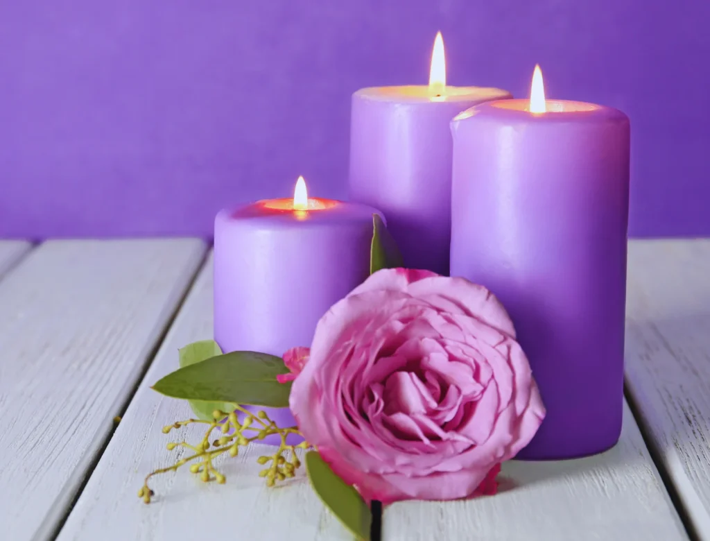 Three candles and a rose on a table.